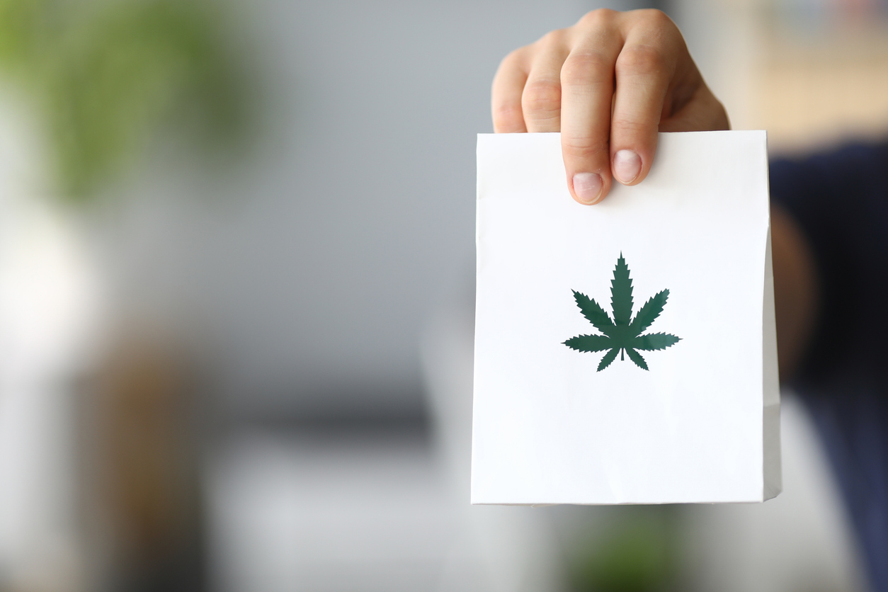 Cannabis delivery - A courier holding out a package of cannabis to a client.